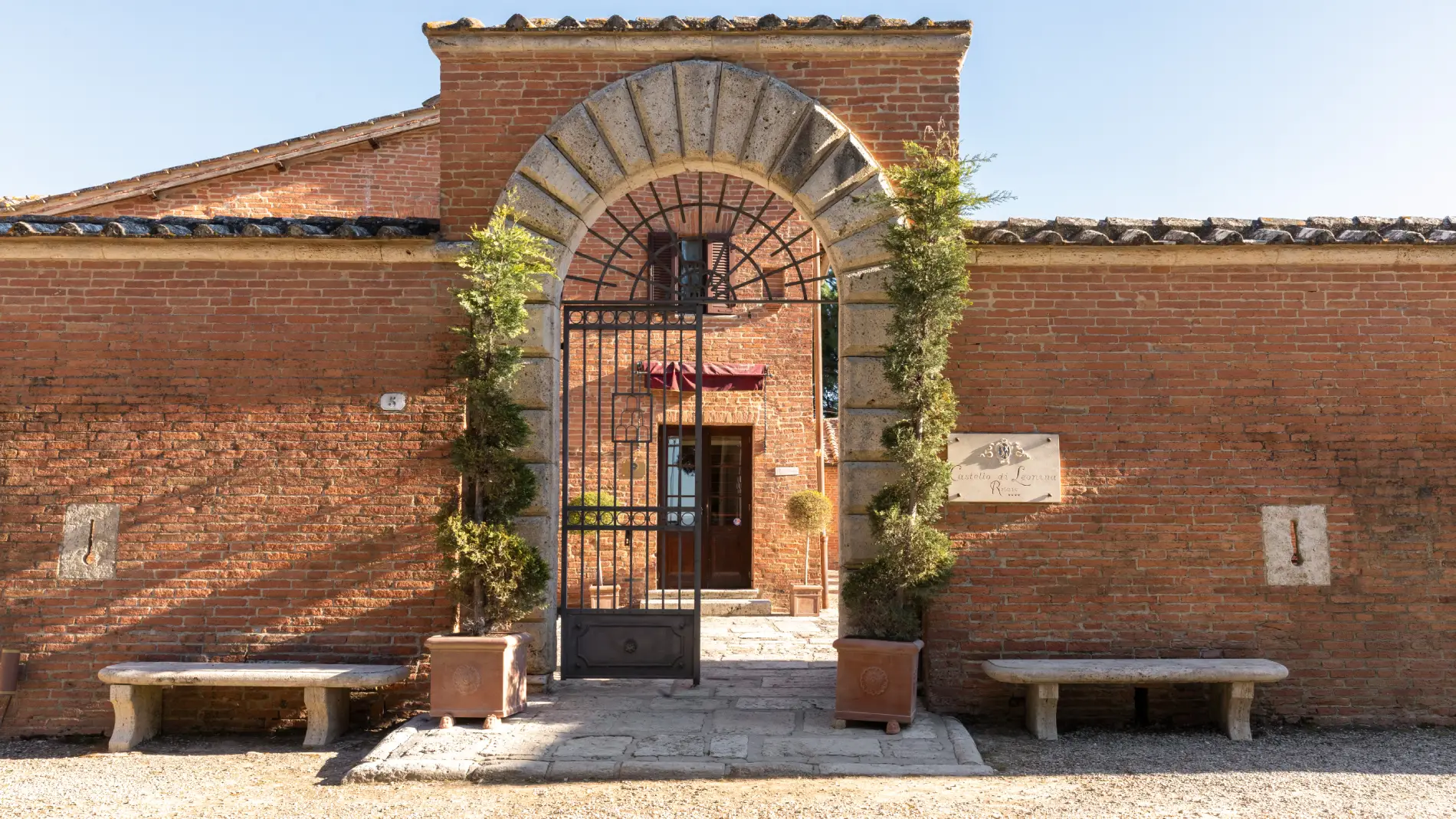 Entrance of Castello di Leonina with stone arch, iron gate and brick facade in Asciano - Castello di Leonina, BZAR hotels in Tuscany
