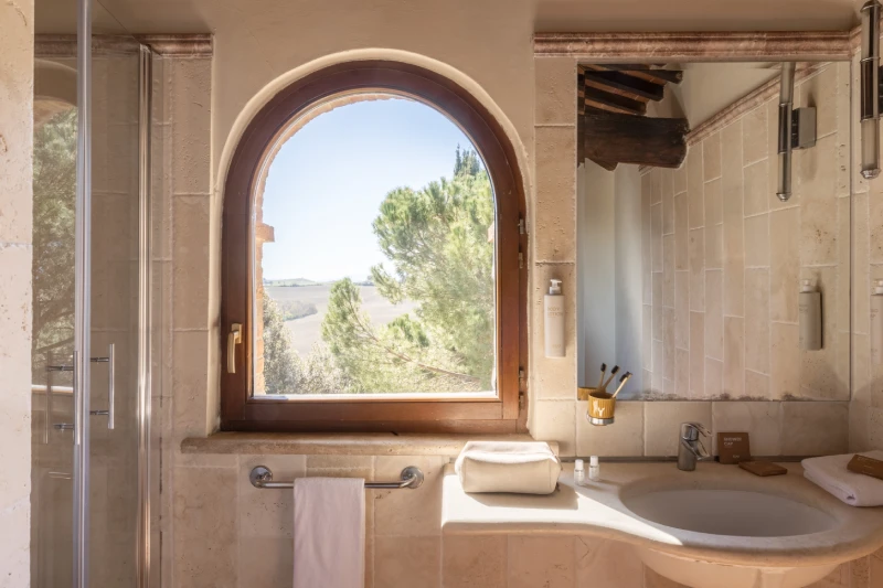 Suite bathroom with large panoramic window, shower and stone sink overlooking the Tuscan countryside of Asciano - Castello di Leonina, BZAR hotels in Tuscany