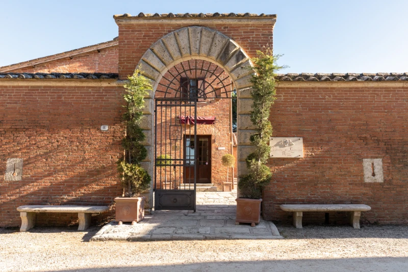 Entrance of Castello di Leonina with stone arch, iron gate and brick facade in the heart of Asciano - Castello di Leonina, BZAR hotels in Tuscany